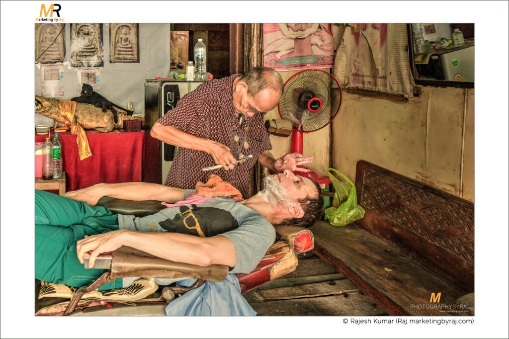 Older Barber shaving a man. Man being shaved at a barbers shop, Bangkok, Thailand